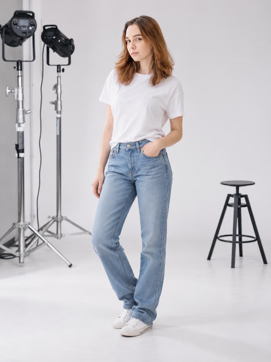 Mia in light-wash straight-leg jeans and a white tee in a white photo studio, one hand in her pocket